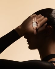 Model in the shadow from the side holding a Serpenti Seduttori rose gold watch with diamonds.