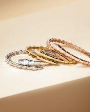 Three Serpenti Viper bracelets in white, yellow and rose gold, light and shadow background.