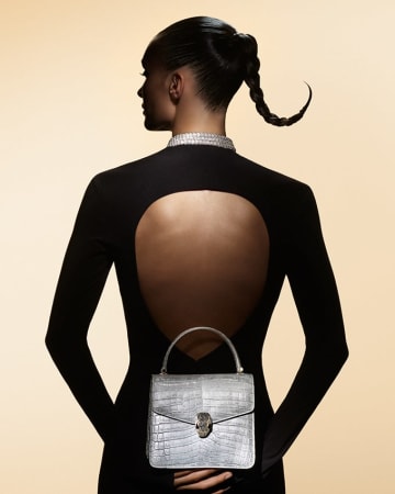Model in the shadow from the back holding a Serpenti Forever Top Handle bag in silver alligator skin.