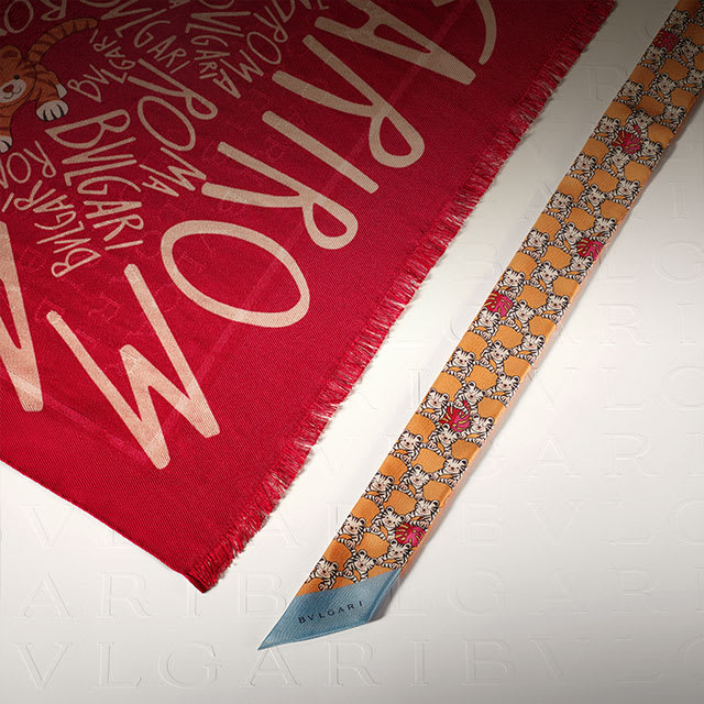 Close-up of a colourful silk foulard with Bvlgari letters on a white Bvlgari logo backdrop.