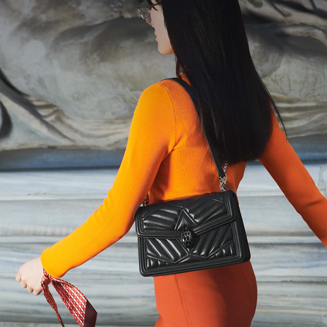 Model holding a Serpenti Diamond Blast shoulder bag in black quilted nappa leather body.