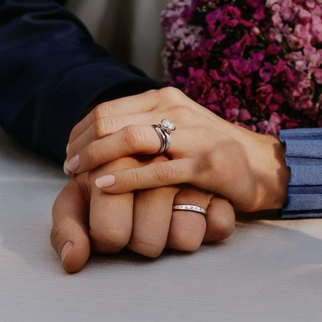 Female and male hands wearing a Bulgari engagement ring and wedding band.