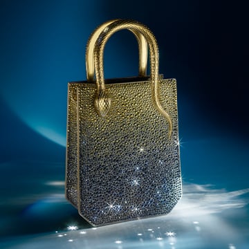 Serpenti Reverse white calf leather bag with metallic handle and snakehead closure against a night sky backdrop.