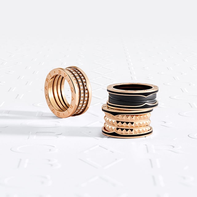 Hand wearing Bvlgari B.zero1 Rock rose gold rings with black ceramic and a studded spiral, and a B.zero1 rose gold ring with diamonds.