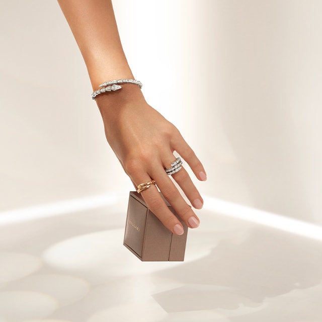 Hand with B.zero1 rings and bracelets holding a Bulgari gift box and B.zero1 four-band rose gold ring.