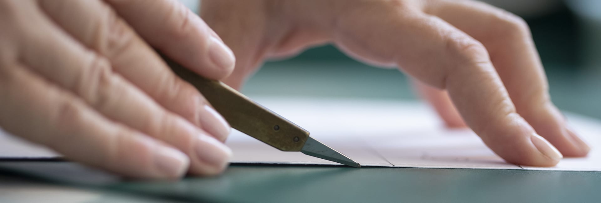 Craftsman cutting a calf leather panel during the making of a Bulgari bag, close-up of the hands.