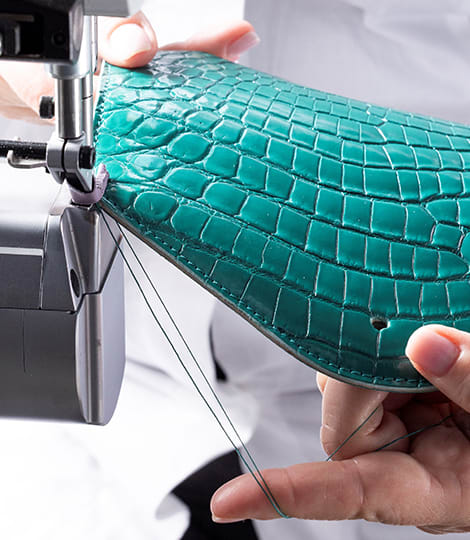Craftsman sewing a crocodile skin panel during the making of a Bulgari bag, close up of the hands.