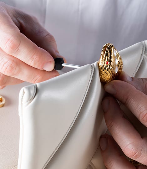 Artisan fixing the snakehead closure of the Serpenti Cabochon bag in white calf leather, close up.