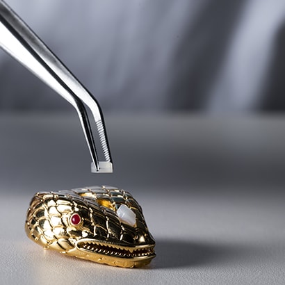 Artisan hand-setting a gem on the heritage snakehead closure of Bulgari's bags, close up.