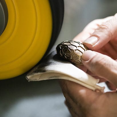 Artisan polishing the iconic snakehead closure of Bulgari's handbags and accessories, close up.