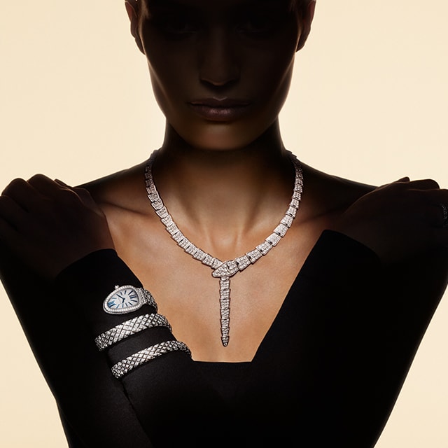 Model wearing a white gold Serpenti necklace and a two-coil bracelet set with diamonds, close up.