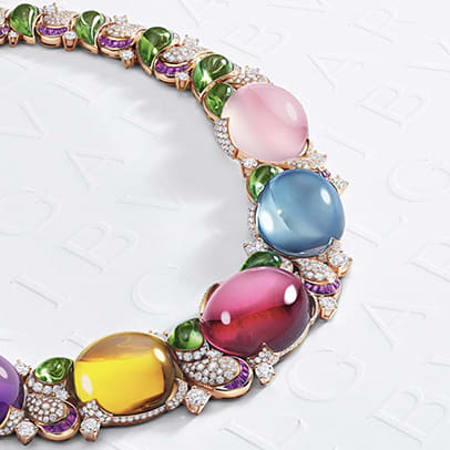 Magnifica High Jewelry rose gold necklace with cabochon amethyst, citrine, rubellite, blue topaz and pink quartz, diamonds and green tourmalines on white Bvlgari logo backdrop.