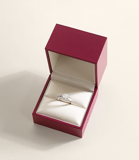 Кольцо для помолвки Torcello из платины с бриллиантом круглой огранки внутри красного футляра.