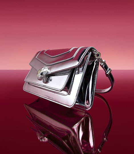 Serpenti Forever bag in silver mirror calf leather with snakehead closure, dark red backdrop.