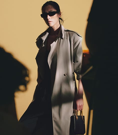 عارضة تحمل حقيبة يد «سيربنتين فيرتيكال» من جلد الغالوشا الأسود الماسي المغبر، على خلفية رمادية.