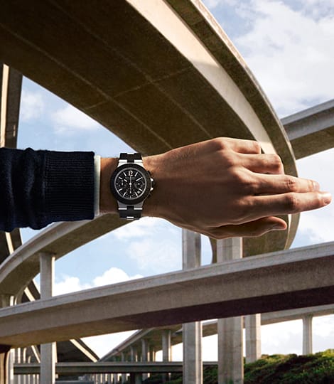 Male arm with Bulgari Aluminium Chronograph watch in black rubber and aluminum, sky backdrop.