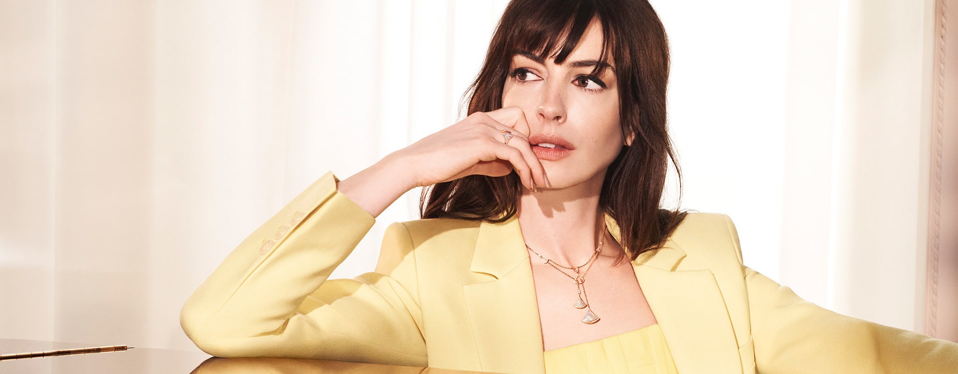 Anne Hathaway leaning against a piano and wearing a yellow gold Divas' Dream necklace and earrings.