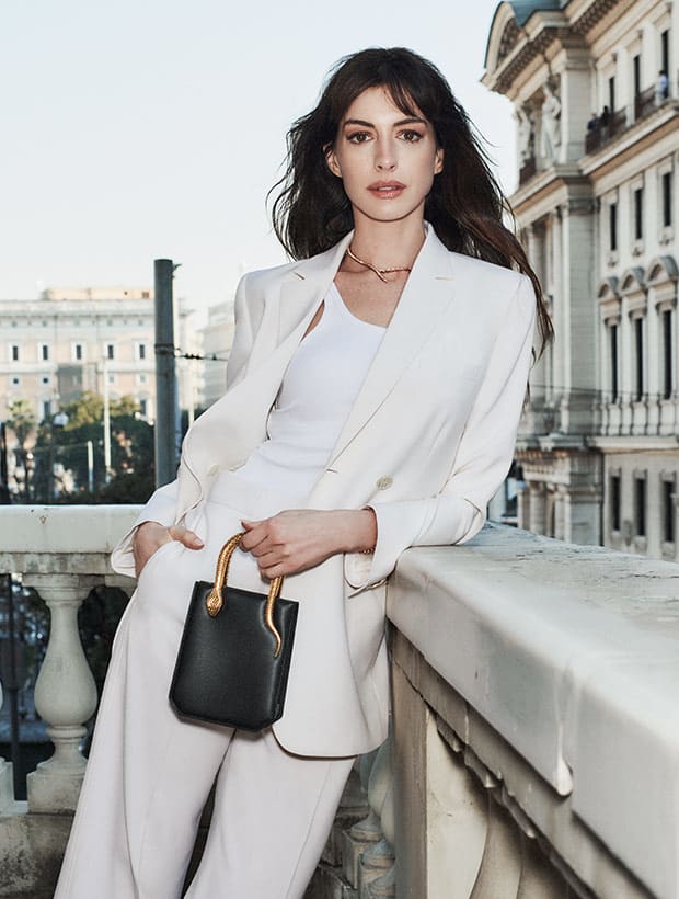 Anne Hathaway holding a small Serpentine Vertical Tote bag in Diamond Dust Galuchat, Roman backdrop.