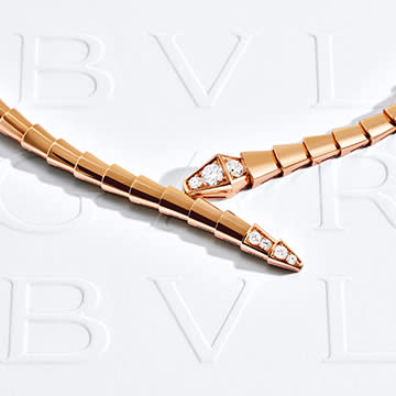 Serpenti Viper rose gold necklace with diamonds on the head and tail, white Bulgari logo backdrop.