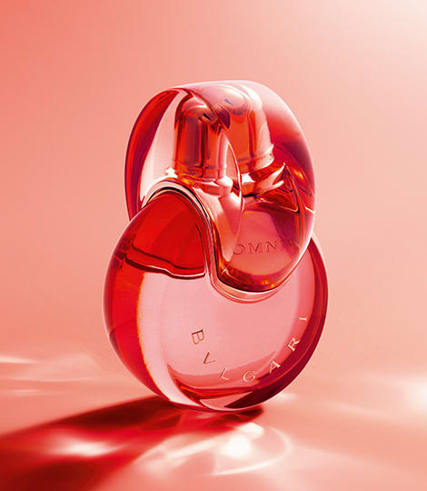 Red Omnia Coral fragrance bottle with Bulgari logo, red backdrop, close-up.