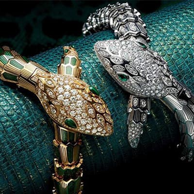 Serpenti secret watches in yellow and white gold with diamonds and coloured gems, green backdrop.