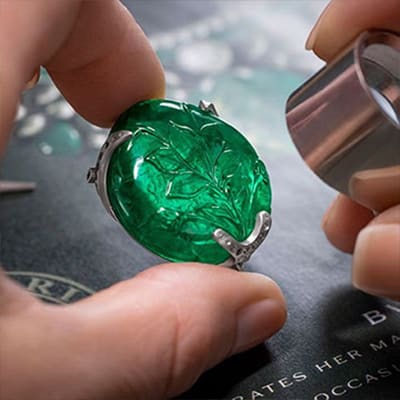 Emerald being analysed through a lens with sketch of a necklace and emeralds in the background, close up.