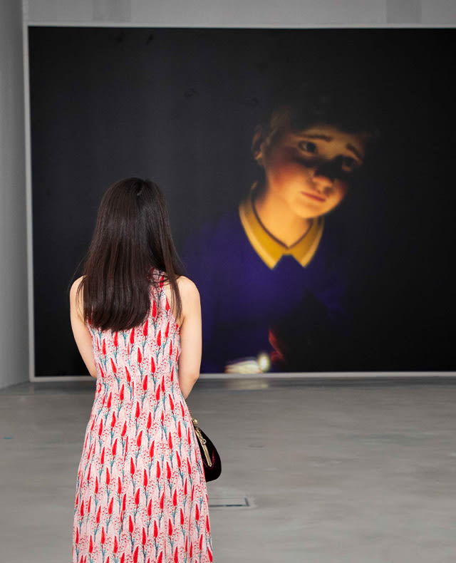 People from behind admiring a painting representing a person in a museum.
