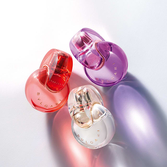 Omnia Crystalline, Omnia Amethyste and Omnia Coral fragrance bottles against a white, purple and red background.