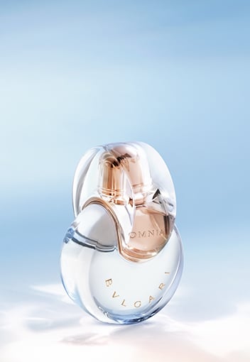 Transparent Omnia Crystalline fragrance bottle with Bulgari logo, sky backdrop, close-up.