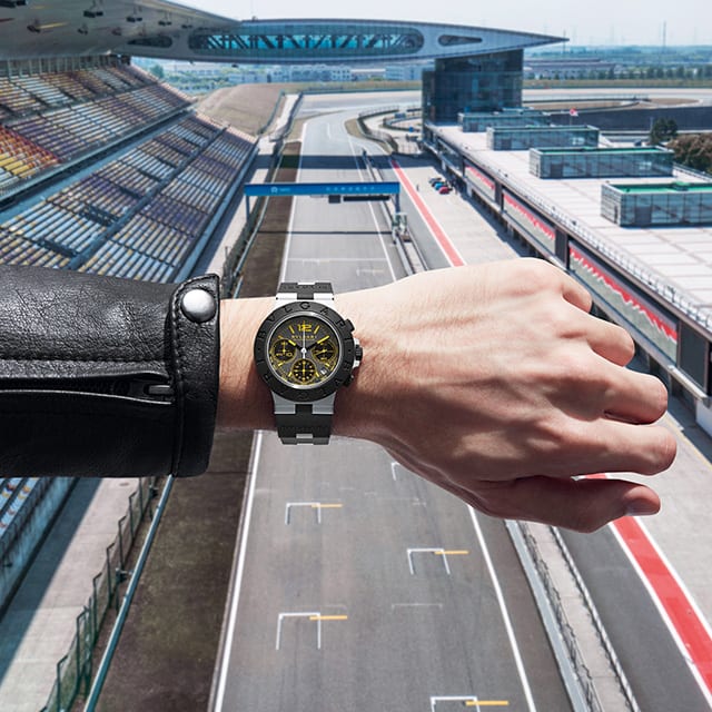 Bulgari Aluminium Gran Turismo Special Edition watch on a man's wrist, racetrack in the background.