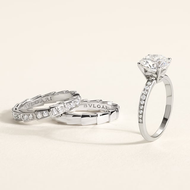 Modella con anello di fidanzamento Bulgari. Fedi nuziali e anello solitario su sfondo bianco.