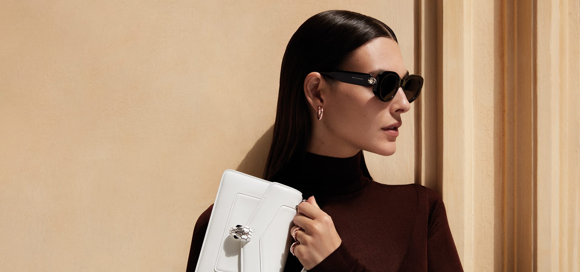 Woman wearing Serpenti Forever black acetate sunglasses and holding a white Serpenti Forever bag.