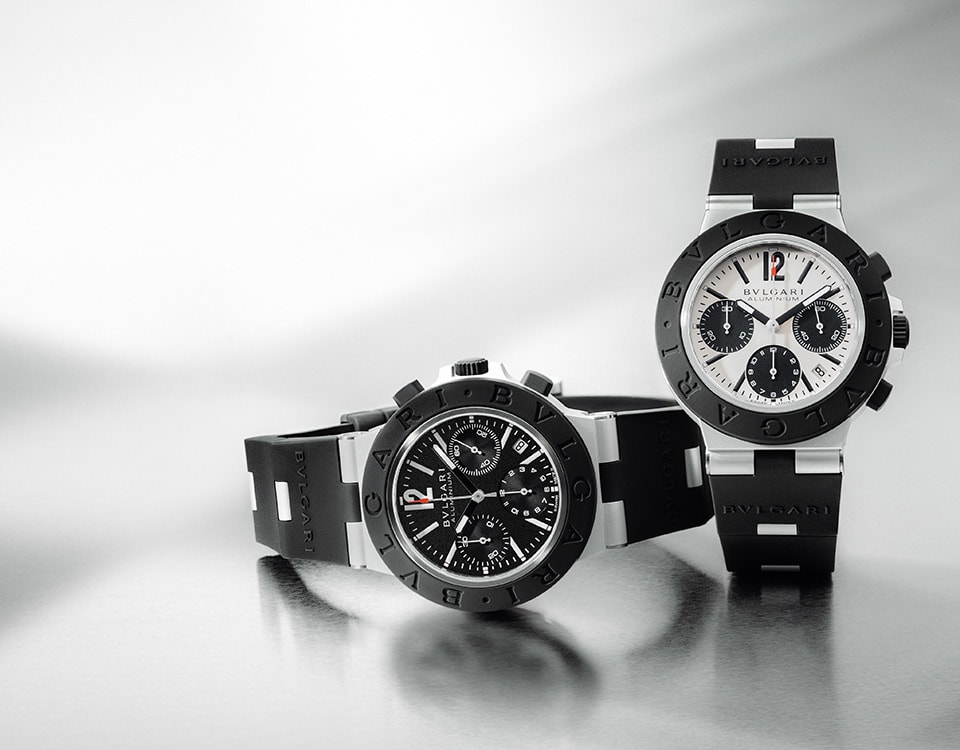 Bvlgari Aluminium watches, one with chronograph function, in aluminum and black rubber, gray backdrop.