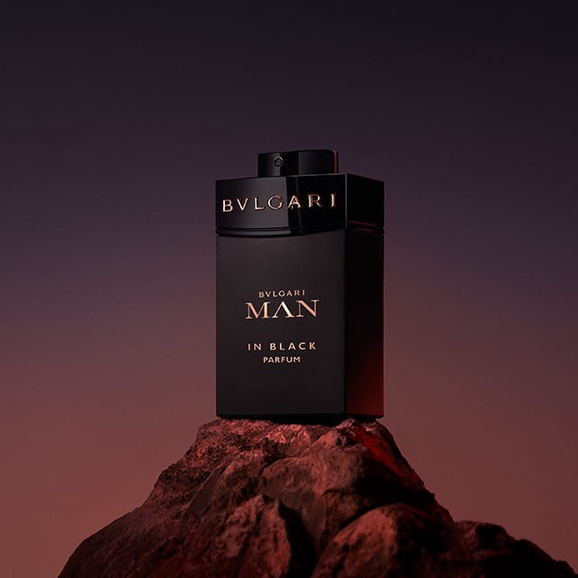 Flacon noir Bvlgari Man in Black Eau de Parfum posé sur un rocher, avec un ciel violet en arrière-plan. Photographie en plan serré.