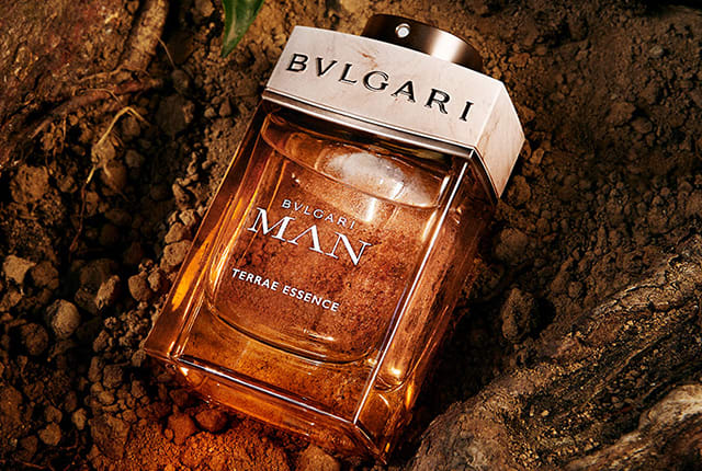 Lorenzo Viotti sitting on the ground holding Bulgari Man Terrae Essence, close up of the perfume.