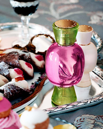Model holding the Bvlgari Dolce Estasi Allegra fragrance flacon in pink and green glass, and wearing a High Jewellery bracelet with coloured gems.