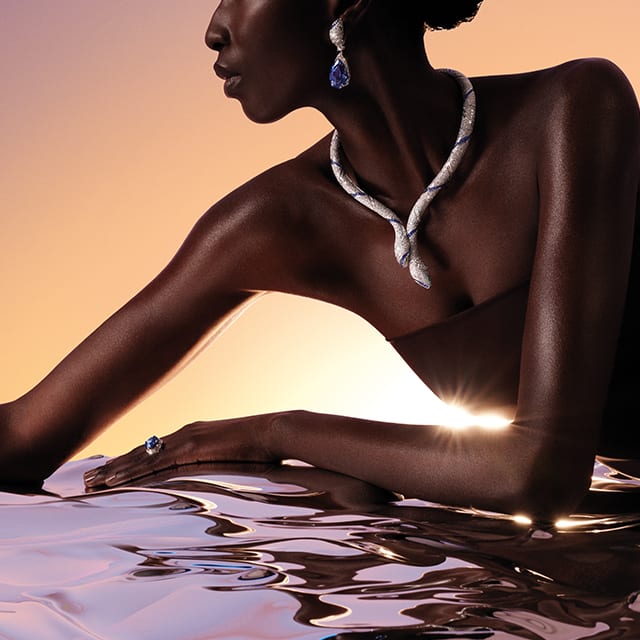 模特兒配戴 Serpenti Sapphire Echo High Jewellery 鑽石項鍊和耳環，背景為黎明時分的天空。 