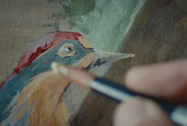 Craftsman hand-painting a colourful bird in the interior of the Bulgari Hotel Rome, close up.