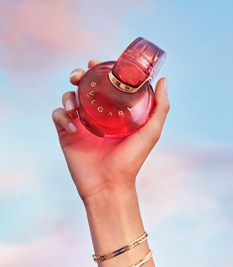 Red Omnia Coral fragrance bottle with Bulgari logo, red backdrop, close-up.