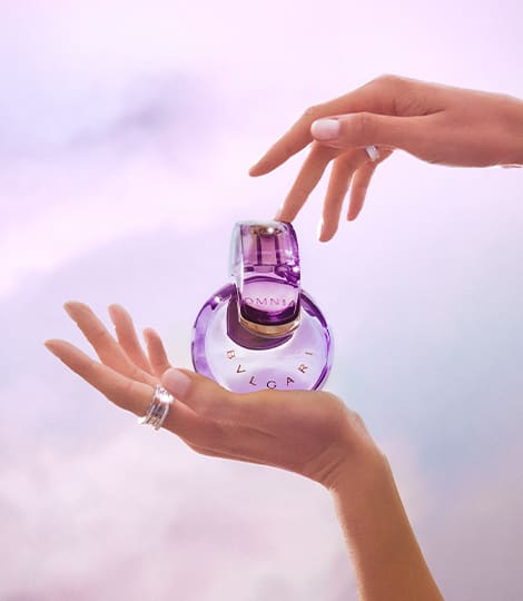 Purple Omnia Amethyste fragrance bottle in the infinity shape, purple backdrop, close-up.