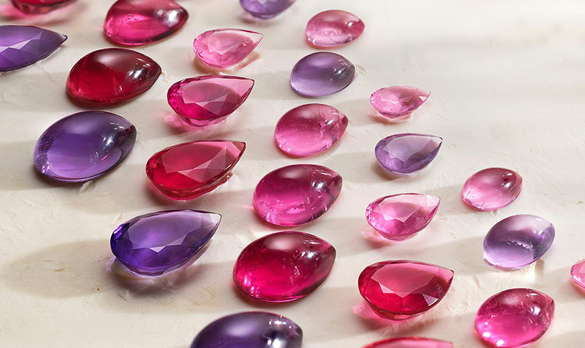 A Bulgari cushion-cut ruby held by tweezers, dark background, close up.