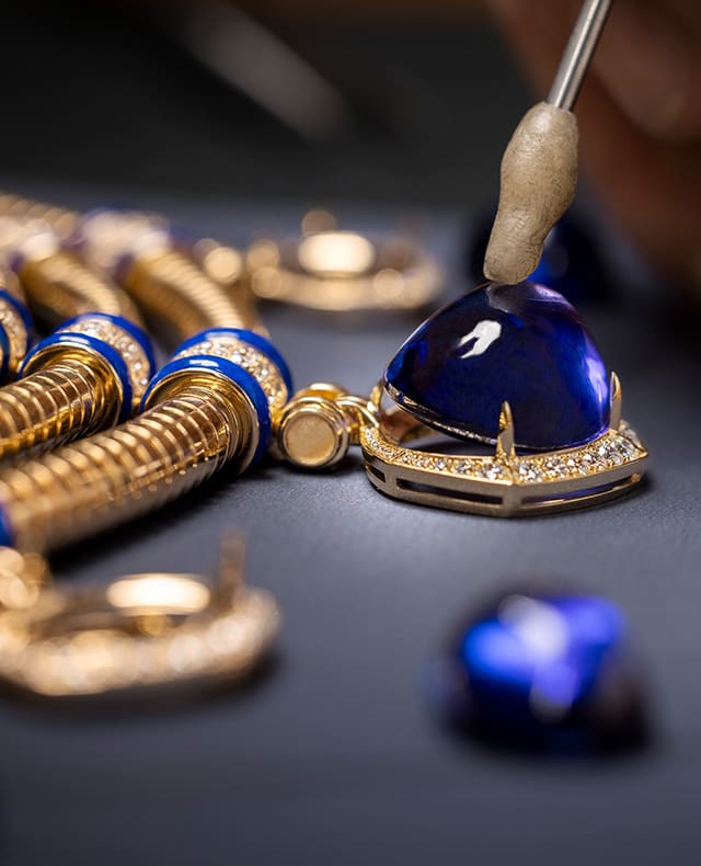Craftsman placing a coloured gem with a tweezer on the sketch of a Bulgari necklace with flowers, close up.