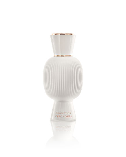 White flacon of the Bvlgari Allegra Magnifying Patchouli essence in front of a patchouli leaf, creative shot.