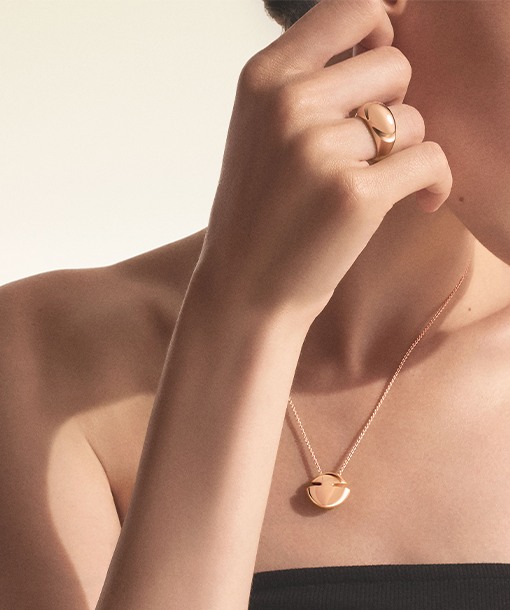 Model wearing a Bulgari Cabochon ring and pendant necklace in 18 kt yellow gold on the skin, close up.